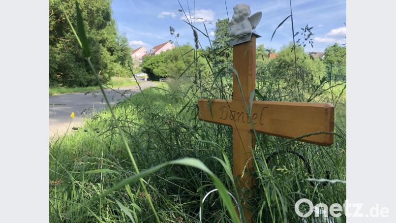 &quot;Daniel&quot; steht auf einem Holzkreuz und erinnert an den 24-Jährigen, der im Sommer 2020 nachts auf seinem Rad auf einem unbeleuchteten Weg nach Hause fuhr, als er im Dunkeln angegriffen und mit einem Messer getötet wurde. Seit 11. Juni steht etwas mehr als hundert Meter vom Tatort entfernt, neben einer viel befahrenen Straße, ein Plakat mit einem Foto des 24-Jährigen. Daneben steht der Satz: «Wer hat mich hier ermordet?» (zu dpa «Wer hat mich hier ermordet?» - Familie hofft auf Antworten&quot;) +++ dpa-Bildfunk +++ Bild: Gregor Bauernfeind/dpa