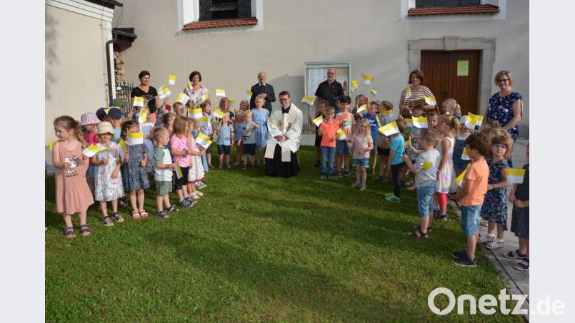Neupriester Bastian Neumann nahm sitzend die Glückwünsche der Fähnchen schwenkenden Kinder des Kinderhauses „Mutter vom guten Rat“ entgegen. Mit dabei im Hintergrund Kinderhausleiterin Imke Steinert (Zweite von rechts), links daneben Pfarrseelsorger Pater Benedikt Leitmayr und der Amberger Regionaldekan Ludwig Gradl. Bild: jr