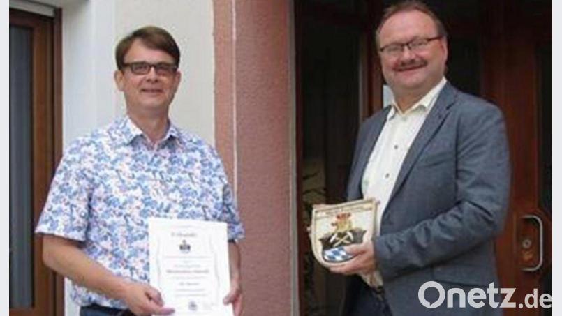 Bürgermeister Uwe König (rechts) gratuliert Amtsrat Max Heindl zum Dienstjubiläum mit Urkunde und Gemeindewappen. Bild: bk
