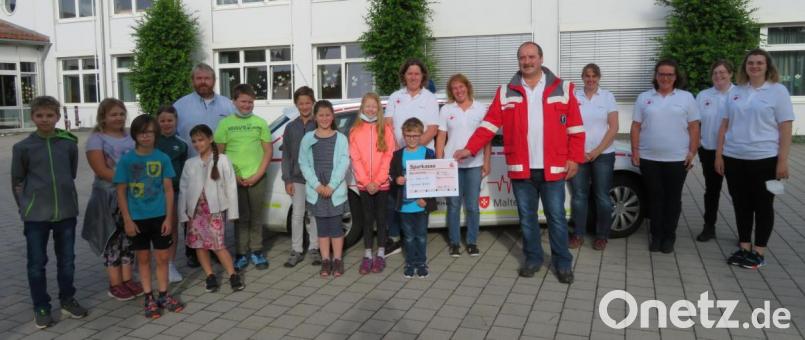 Pfarrer Albert Hölzl und die Schüler der vierte Klasse übergaben die Spende an die Helfer-vor-Ort-Gruppe Tiefenbach. Nikolaus Scherr (mit Sanitätsjacke) bedankte sich namens des Fördervereins. Bild: nis