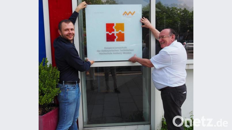 Schulleiter Josef Weilhammer (rechts) zeigt die neue Kooperationstafel zusammen mit Michael Abler als Vertreter der Elektronik-Fakultät der OTH Amberg-Weiden. Bild: Bühner