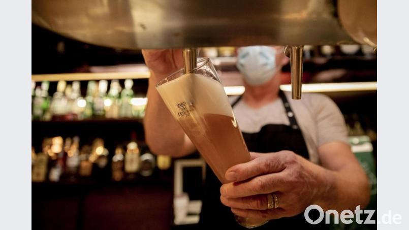 Ein Wirt mit Maske zapft in einer Kneipe ein Bier. Symbolbild: Christoph Soeder/dpa