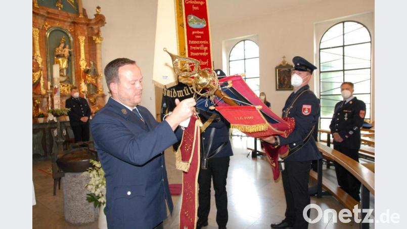 Vorsitzender Christian Renghart heftet das Fahnenband an die Fahne des Patenvereins Dietldorf. Bild: pop