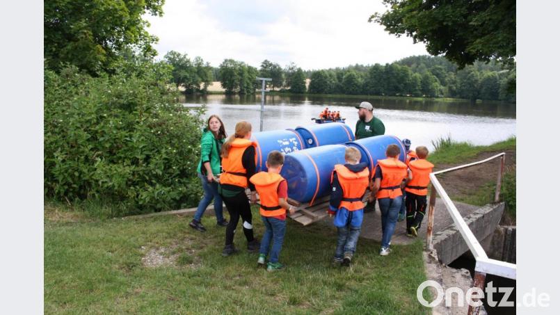 Gemeinsam bugsieren Erzieher und Kinder das Floß vom Dorfplatz zum gleich nebenan gelegenen Heindlweiher: Spielerisches Sozialkompetenztraining im Team steht bei den &quot;Lerning Campus&quot;-Ferienfreizeiten als Lernziel an oberster Stelle. Bild: bjp