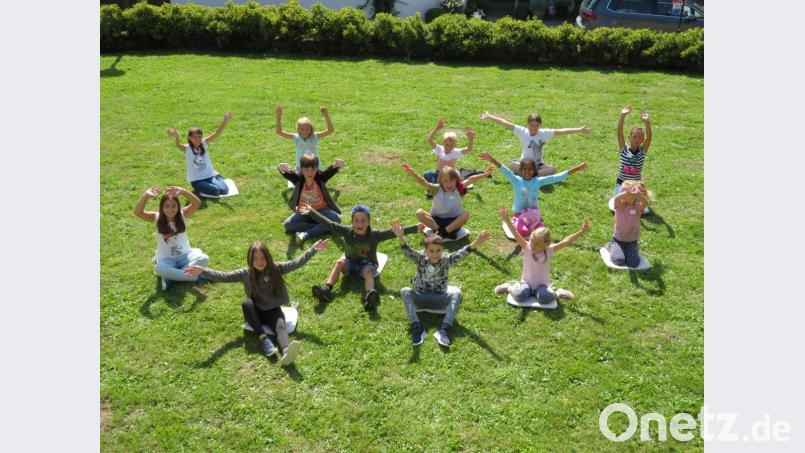 Geschafft. Nach dem Anfertigen der Tonplastiken entspannen die Kinder auf der Wiese und strecken ihre Arme wie Fühler nach oben. Bild: adj