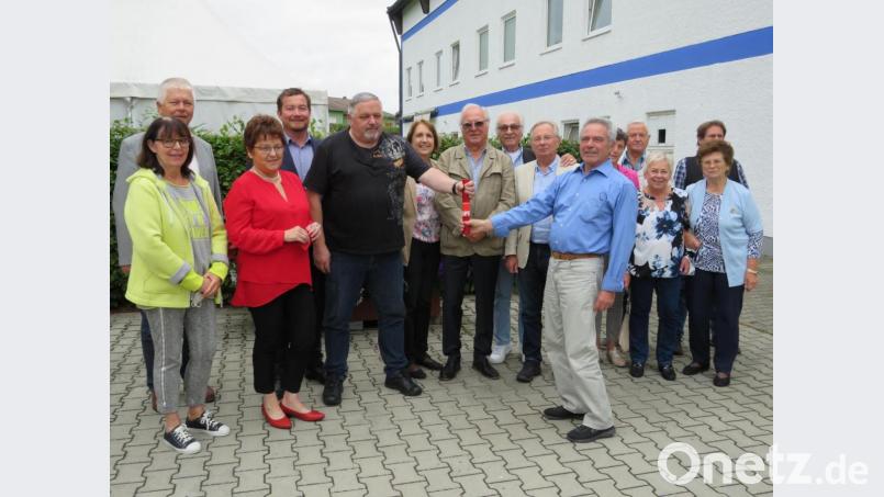 Symbolisch überreichte Helmut Fastner(rechts) den „roten Staffelstab“ an seinen Nachfolger Heinrich Rewitzer. Die weitere Vorstandschaft und Gäste gratulierten. Bild: adj