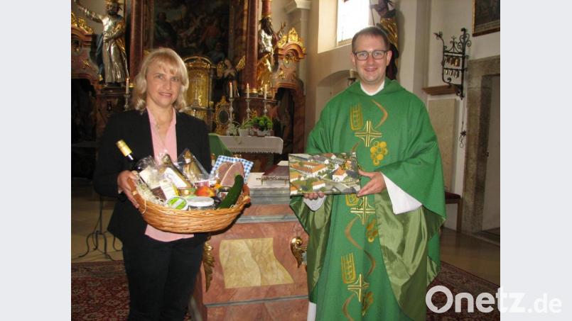Mit einem Luftbild der Pfarrkirche und einem Korb mit regionalen Spezialitäten bedankte sich Pfarrgemeinderatssprecherin Bettina Schmid bei Kaplan Daniel Fenk. Bild: Pfarramt Wondreb/exb