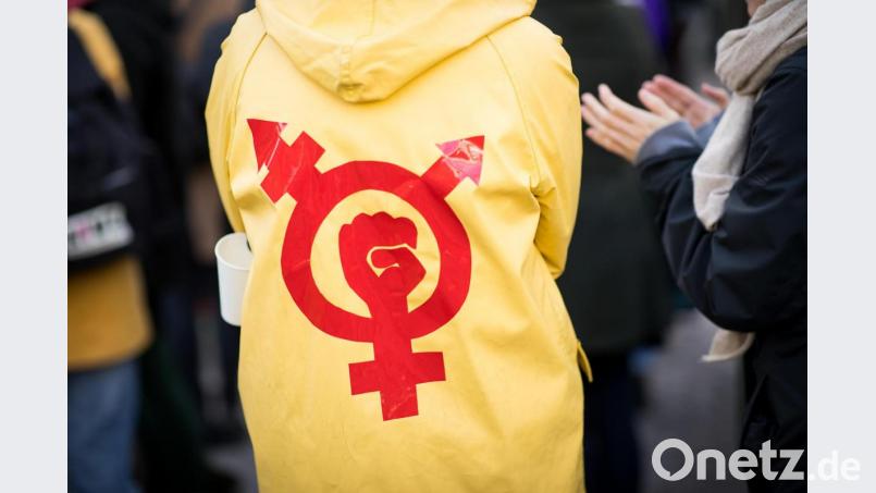 Eine Frau trägt einen gelben Regenmantel mit einem Gender- und Protestsymbol bei einer Kundgebung zum Internationalen Frauentag. Symbolbild: Christian Charisius/dpa