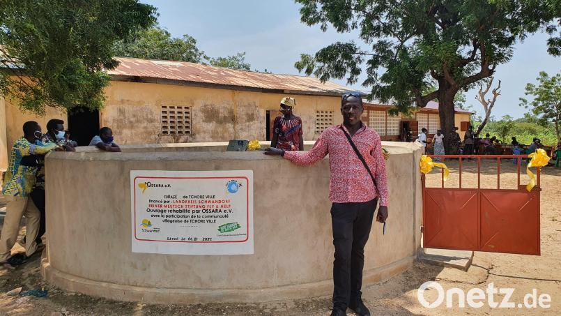 Ein Mitarbeiter des Projektpartners Ossara e.V. steht vor dem sanierten Pumpbrunnen mit der Spendentafel. Im Hintergrund ist die alte sowie die neue Schule erkennbar. Bild: Ossara e.V./exb