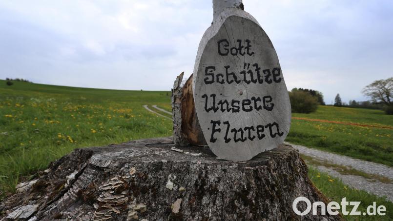 An einem auf einem Baumstumpf stehenden Kreuz lehnt eine Holzscheibe mit der Aufschrift &quot;Gott schütze unsere Fluren&quot;. Symbolbild: Karl-Josef Hildenbrand/dpa