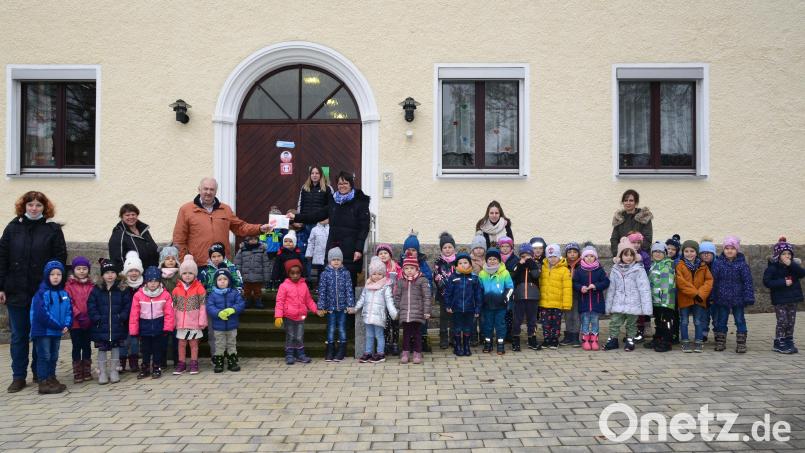 Kindergartenleiterin Beate Schuch (auf der Haustreppe, rechts) übergibt dem Vorsitzenden der Kinderkrebshilfe Oberpfalz Herbert Putzer den am Martinstag in der Andacht gesammelten Betrag von 230 Euro. Bild: bey