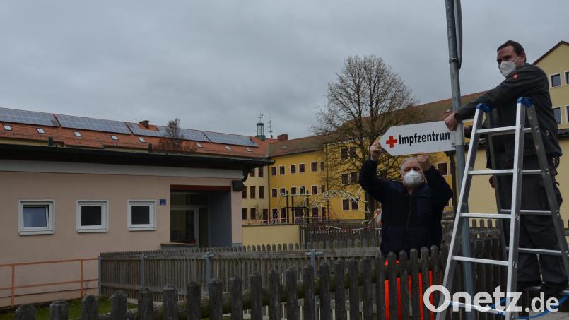 BRK-Helfer Heinrich Rewitzer (links) und Grundschulhausmeister Thomas Beierl bringen am Montag das Schild &quot;Impfzentrum&quot; vor der Eglsee-Turnhalle in Vohenstrauß an. Hier wird nun wie schon im Frühjahr geimpft: Bis 30. November dienstags und mittwochs, danach montags bis freitags. Bild: dob