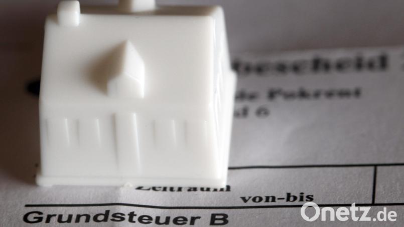 Ein kleines Spielzeughaus steht auf einem Bescheid zur Grundsteuer. Symbolbild: Jens Büttner/dpa