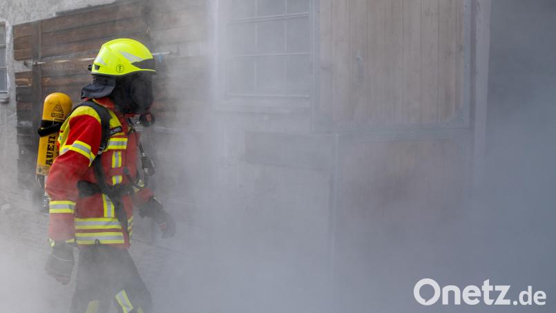Ein Feuerwehrmann mit Atemschutzausrüstung geht zu einem früheren Kuhstall, aus dem Rauch dringt, um darin zu üben. Symbolbild: Stefan Puchner