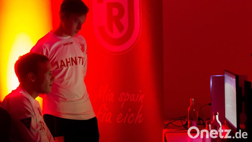 Sven Kopp (sitzend) in Aktion an der Konsole, Leon Kipry als Beobachter und Tippgeber: Die beiden Fußballer der SpVgg SV Weiden zocken in ihrer Freizeit in der &quot;Virtual Bundesliga&quot; für den SSV Jahn Regensburg. Bild: SSV Jahn Regensburg