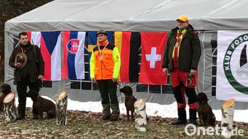 Stephan Vogl (Dritter von links mit seinem Rüden “Enok vom Dorngraben”) kann stolz auf den Erfolg sein. Das Bild zeigt ihn vor der Deutschlandfahne bei der Siegerehrung im polnischen Radomierowice. Bild: Stephan Vogl/exb