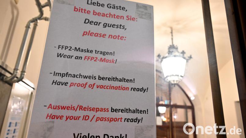 Ein Schild mit der Aufschrift "Liebe Gäste, bitte beachten Sie: FFP2-Maske Tragen! - Impfnachweis bereithalten! - Ausweis/Reisepass bereithalten! - Vielen Dank!" hängt in Deutsch und Englisch am Eingang zu einer Gaststätte. Symbolbild: Peter Kneffel