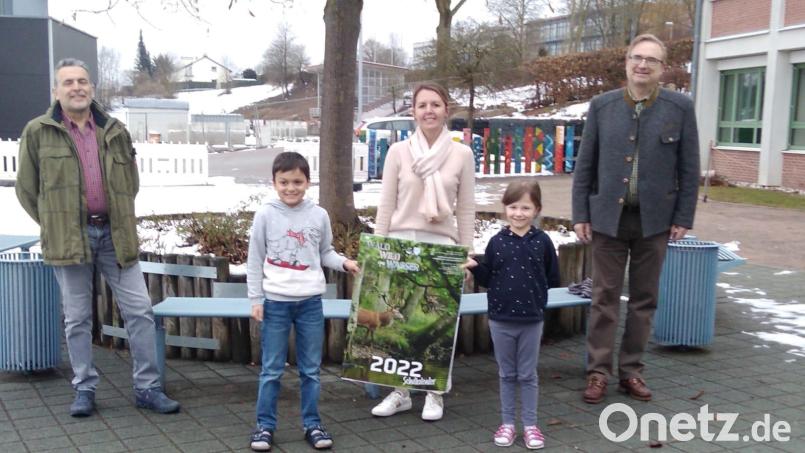Die Kinder der dritten Klasse nahmen den Kalender &quot;Wald, Wild und Wasser 2022&quot; aus den Händen von Landtagsabgeordnetem Alexander Flierl (rechts) und Rainer Mösbauer von der Hegegemeinschaft Oberviechtach (links) entgegen. Konrektorin Stefanie Hauser bedankte sich. Bild: wel