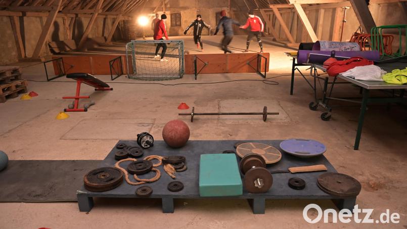 Auf dem Dachboden der alten Scheune stehen und liegen Fitnessgeräte herum, im Hintergrund spielen Fußballer von Germania Amberg drei gegen drei auf einem Mini-Feld. Bild: ref