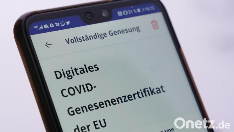 Ein Mann hält sein Smartphone mit einem digitalen Covid-Genesenenzertifikat vor einem Apotheken-Logo hoch. Symbolbild: Marcus Brandt
