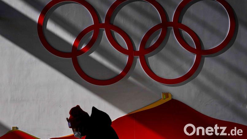 Ein Mann trägt eine Schutzmaske, während er vor Beginn der Wettkämpfe bei den Olympischen Winterspielen 2022 in das Nationale Skisprungzentrum Zhangjiakou geht. Bild: Matthias Schrader/dpa