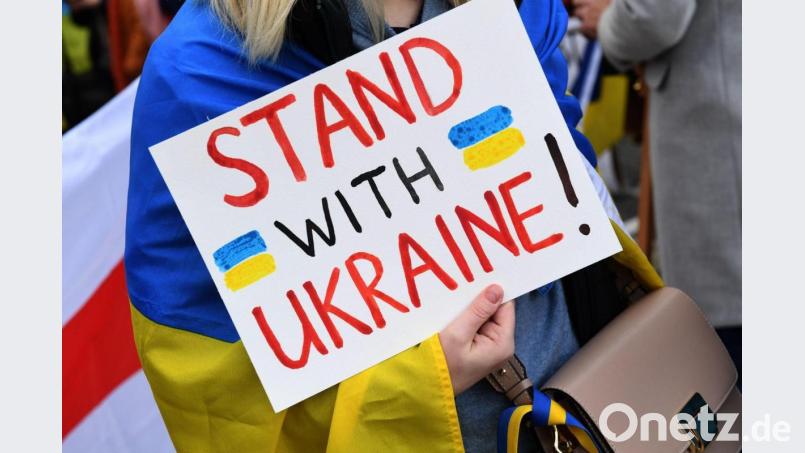 Eine Demonstrantin steht mit einem Plakat "Stand with Ukraine! " steht bei einer Demo. Bild: Felix Hörhager/dpa