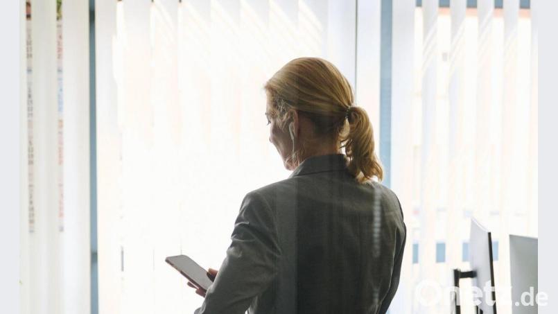 Eine Frau steht in einem Bürozimmer und hält ein Smartphone in der Hand (gestellte Szene). Bild: Annette Riedl/dpa