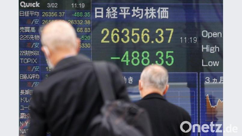 Menschen mit Mund-Nasen-Schutz gehen an einer elektronischen Börsentafel vorbei, die den japanischen Nikkei-Aktienindex anzeigt. Bild: Rodrigo Reyes Marin/ZUMA Press Wire/dpa