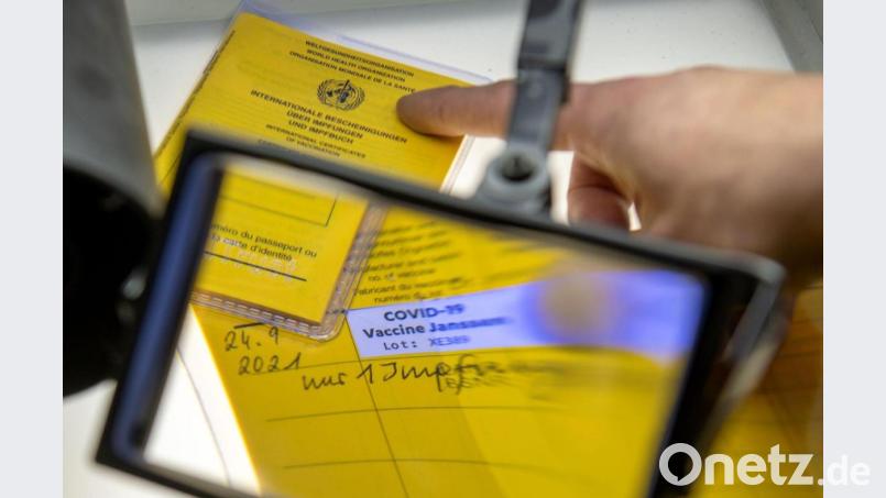 Gefälschte Impfpässe unter einer Lupe (Symbolbild). Bild: Stefan Puchner/dpa