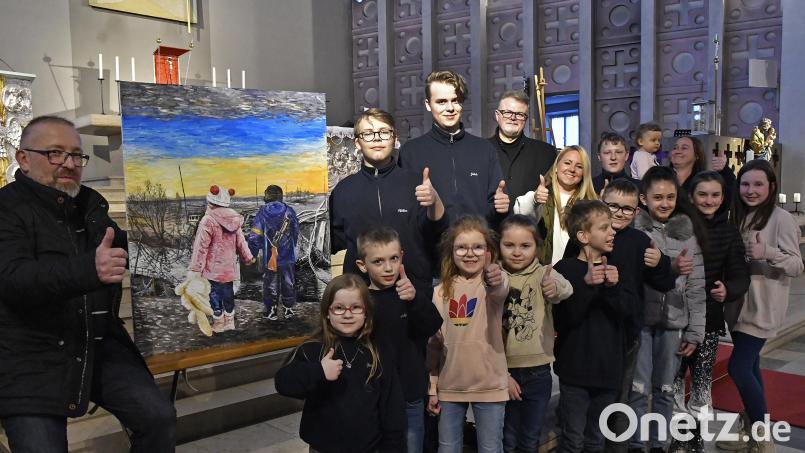 Dieses Motiv ist sinnbildlich für die aktuelle Zerrissenheit der Ukraine. Auf dem Foto sind neben dem Künstler Piotr Chamczyk (links neben dem Bild) und Seelsorger Maciej Kolanowski einige der Ministranten und Gruppenleiterinnen zu sehen, die am Sonntag bei ihrem Kuchenverkauf 1140 Euro eingenommen haben. Bild: Petra Hartl