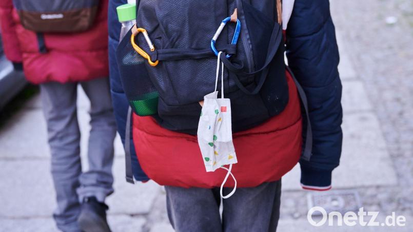 Eine Kindermaske hängt an einem Rucksack eines Schulkindes. Ab Montag fällt die Maskenpflicht in allen Jahrgängen weg. Bild: Annette Riedl/dpa