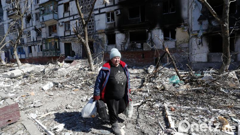 Eine Frau geht am 28. März an einem von russischen Angriffen beschädigten Gebäude in Mariupol vorbei. Symbolbild: -/Victor/XinHua/dpa