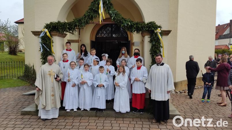 Die Erstkommunionkinder mit Pfarrer Roland Klein und den Ministranten vor der Pforte der Pfarrkirche St. Petrus und Paulus in Neukirchen. Bild: dlu
