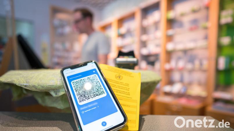 Ein Smartphone mit dem QR-Code eines digitalen Impfausweises liegt zusammen mit einem Impfbuch auf dem Tisch einer Apotheke. Symbolbild: Oliver Dietze