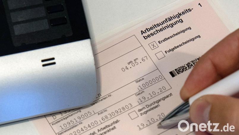 Ein Mitarbeiter einer Arztpraxis notiert etwas auf einer Arbeitsunfähigkeitsbescheinigung. Bild: Paul Zinken/dpa-Zentralbild/dpa/Symbolbild