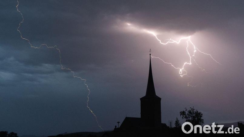 Blitze entladen sich aus einer Gewitterwolke über der Ortschaft. Bild: Nicolas Armer/dpa