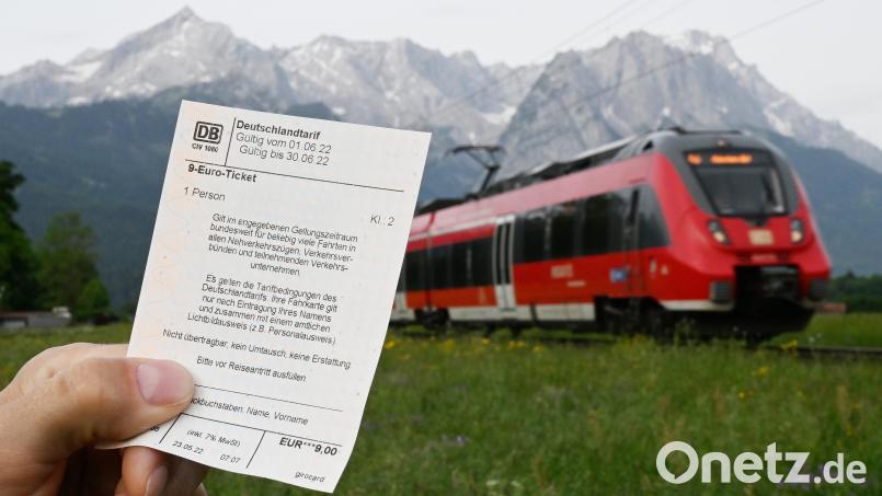 Ein Mann hält ein 9-Euro-Ticket in der Hand, im Hintergrund fährt ein Zug der Deutschen Bahn vor der Bergkulisse des Wettersteingebirges vorbei. Symbolbild: Angelika Warmuth