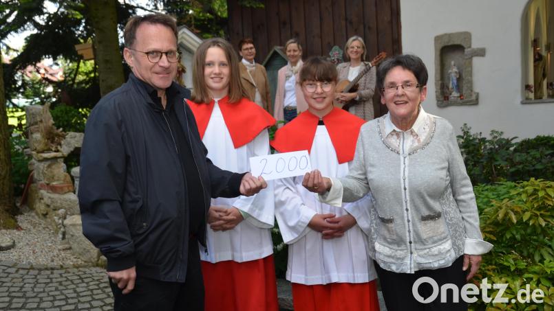 Christa Wildenauer (rechts) zeigt ein großes Herz für die Ministranten in der Pfarrgemeinde. Anlässlich der Maiandacht in der Christophorus-Kapelle mit der Gruppe &quot;TriAngel&quot; aus Waldthurn (im Hintergrund) überreicht sie mit zwei ihrer Enkelkinder an Dekan Alexander Hösl 2000 Euro. Bild: dob