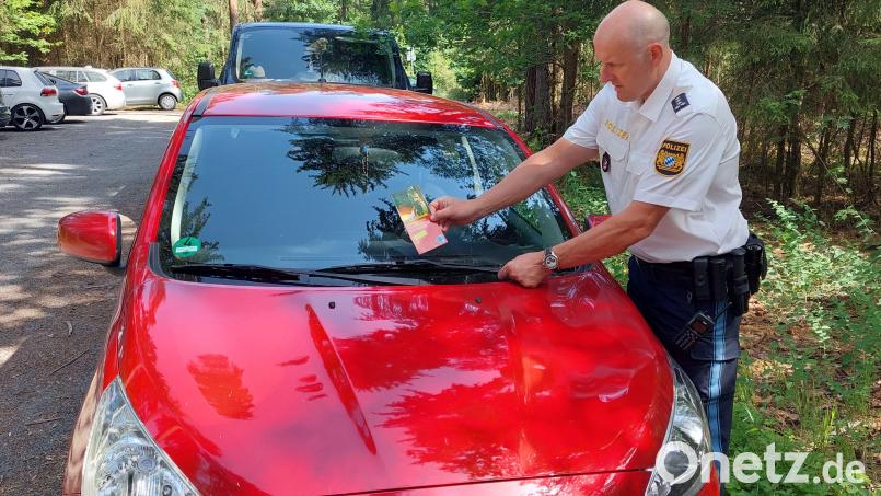 Erster Polizeihauptkommissar Günther Burkhard klemmt ein Flugblatt an die Windschutzscheibe eines parkenden Autos beim Rothenbürger Weiher. Bild: Polizeiinspektion Tirschenreuth/exb