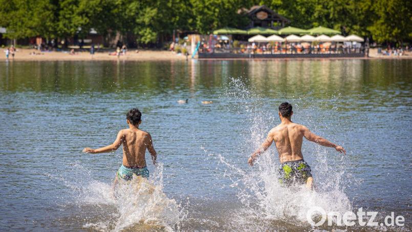 Zwei junge Männer rennen bei sonnigem Wetter in das Wasser eines Sees. Bild: Moritz Frankenberg/dpa/Symbolbild