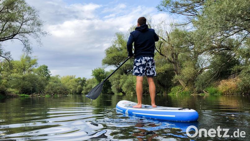 Ein junger Mann paddelt auf einem Stand-Up-Paddling-Board über einen Fluss. Symbolbild: Julian Stratenschulte/dpa