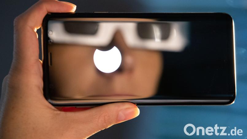 Eine Person mit einer &quot;SoFi-Brille&quot; spiegelt sich im Display eines Smartphones, auf dem eine partielle Sonnenfinsternis zu sehen ist. Die Sternwarte Dieterskirchen ist zu der &quot;SoFi&quot; am 25. Oktober geöffnet. Bild: Friso Gentsch/dpa