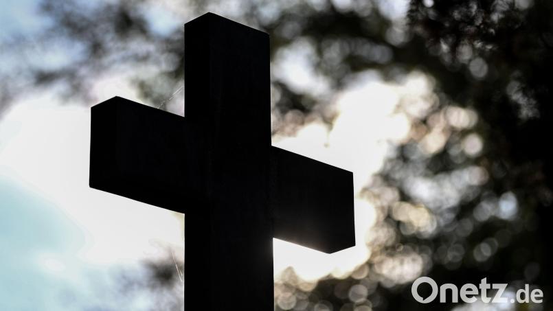Ein Kreuz im Gegenlicht auf einem Friedhof. Zu Allerheiligen möchte ein Senior seiner verstorbenen Jugendfreundin ein Blumengebinde schenken. Doch die Stadtverwaltung kann keine Auskunft darüber geben, wo das Grab auf dem Friedhof zu finden ist. Bild: Patrick Pleul/dpa-Zentralbild