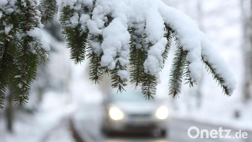 Ein Auto fährt hinter einem schneebedeckten Zweig über die Straße. In Bayern haben sich wegen Schnee und Glätte einige Unfälle ereignet. Symbolbild: Matthias Bein/dpa