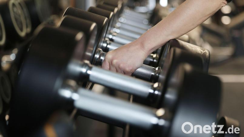 Eine Frau nimmt in einem Fitnessstudio Hanteln aus dem Ständer. Bild: Oliver Berg/dpa/Symbolbild