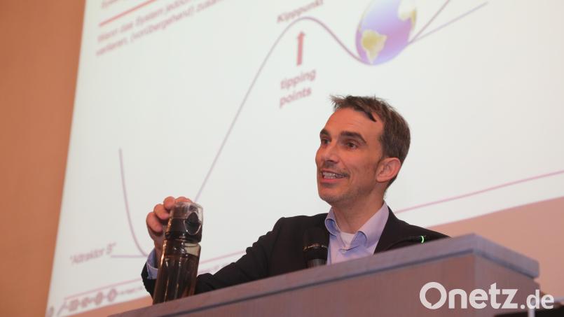 Professor Markus Beckmann erklärt einen Kipppunkt: Irgendwann fällt die Flasche in seiner Hand um. Dann schafft sie es nicht mehr, aus eigener Kraft in ihre Ausgangsposition zurückzukehren. Bild: Wolfgang Steinbacher