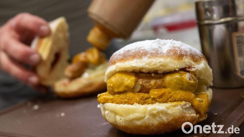 Bäckermeister Florian Perkmann bereitet einen Wurst-Krapfen in seiner Bäckerei zu. Bild: Peter Kneffel/dpa/Archivbild
