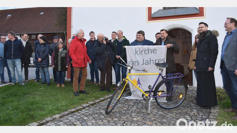 Der 1. Vorsitzende des Fördervereins Simultankirchen in der Oberpfalz, Hans-Peter Pauckstadt-Künkler (rote Jacke), und Sulzbach-Rosenbergs 2. Bürgermeister Günther Koller überreichten vor dem Eingang der Filialkirche St. Margareta die Fahne und das Fahrrad an Illschwangs Bürgermeister Dieter Dehling. Bild: no