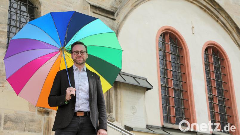 Lucas Lobmeier setzt gerne subtile Botschaften, wie hier mit einem Regenbogen-Schirm vor der Pfarrkirche St. Marien in Sulzbach: „Den Schirm kann jeder deuten, wie er gerne möchte.“ Der Kaplan verlässt die Pfarrei in gut drei Monaten. Bild: Wolfgang Steinbacher