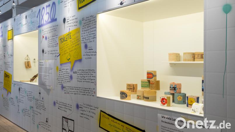Blick in die Ausstellung mit der Wandgestaltung des Illustrators Michael Szyszka. In der Vitrine rechts sind verschiedene historische Klopapiere zu sehen. Bild: Daniel Vogl/dpa